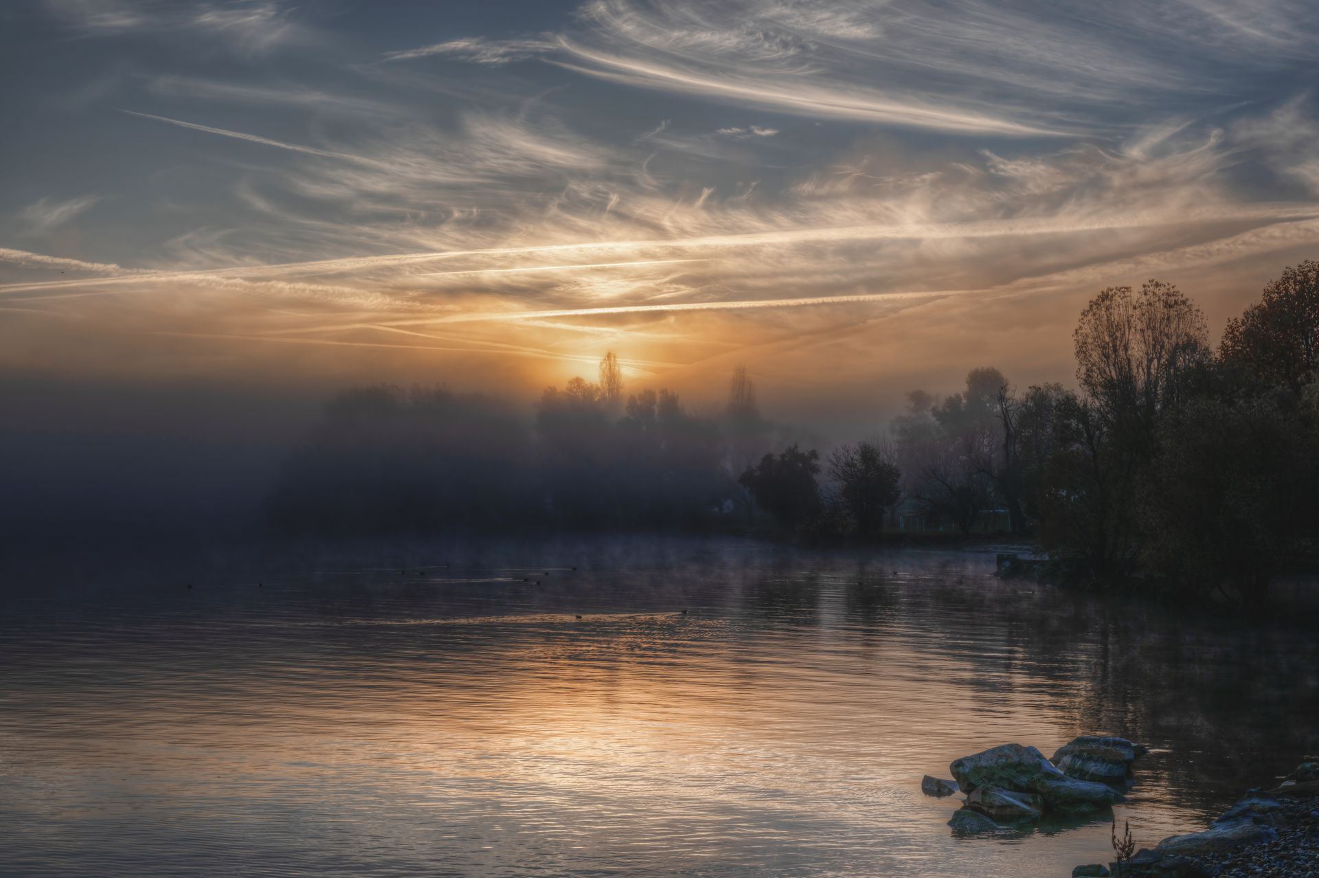 Sunrise light breaking through mist over a still lake at dawn